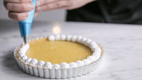 Pâtissier affairé à déposer la crème meringuée à la poche à douille sur la tarte au citron
